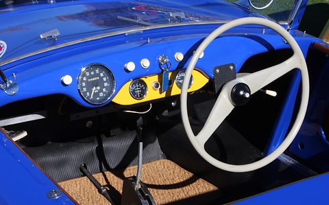 White two-spoke steering wheel and round dials on a blue and yellow dashboard. Opens a larger view