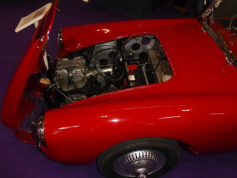 Red sports car with its bonnet open showing the twin-cylinder engine. Opens a larger view