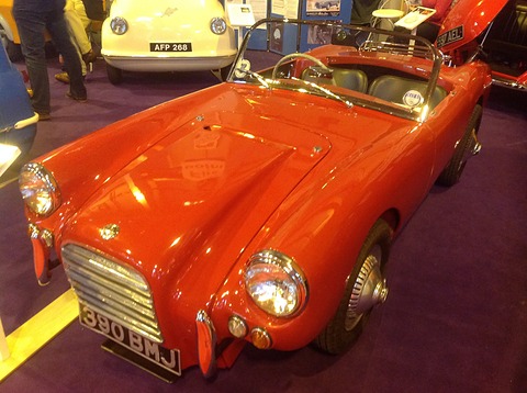 Red open sports car with a vertical-bar grille, on a purple show carpet