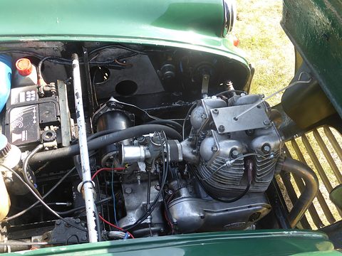 Two-cylinder engine with black and silver castings inside a green engine bay. Opens a larger view