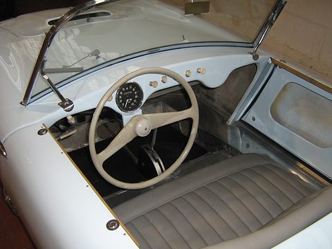 Cream two-spoke steering wheel, a single round speedometer and a grey bench in a white body. Opens a larger view