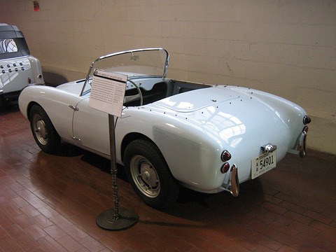 White open two-seater from behind beside an information stand on a brick floor. Opens a larger view