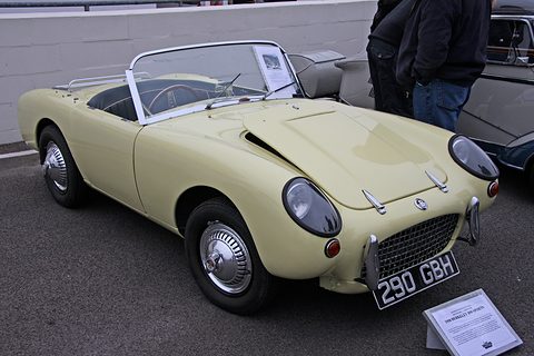 Cream open two-seater on tarmac seen from the front right, an information board beside. Opens a larger view