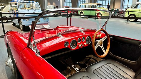 Wood-rimmed steering wheel and a row of round dials on a red dashboard. Opens a larger view