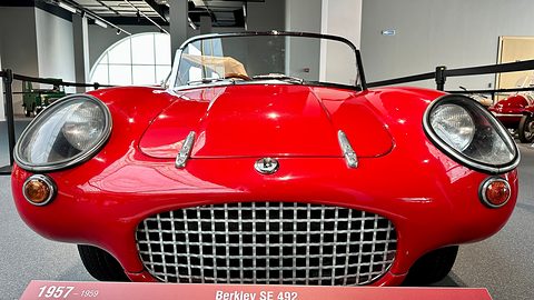 Front of a red sports car with a wide wire-mesh grille and two headlamps, a museum label below. Opens a larger view