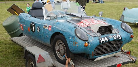 Blue three-wheeler with race number 77 on a trailer, engine exposed at the front. Opens a larger view