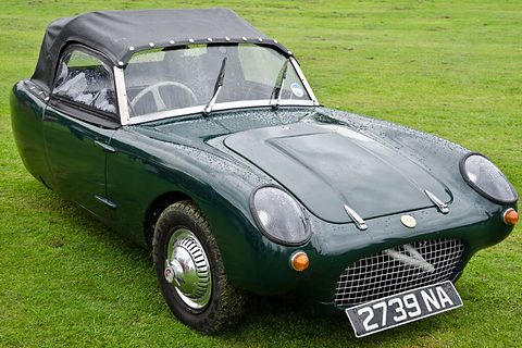 Dark green three-wheeler with a black hood, seen from the front right on grass. Opens a larger view