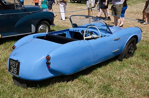Blue three-wheeler from the rear on grass, its single rear wheel tucked under the tail. Opens a larger view