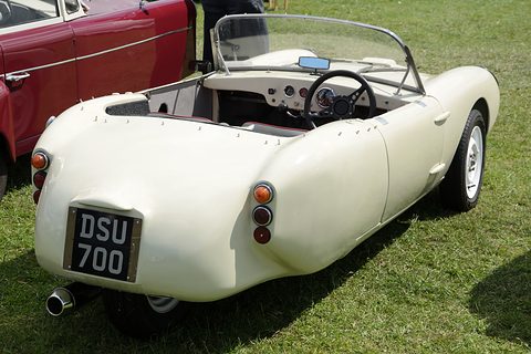 Cream three-wheeler seen from behind on grass, chrome exhaust under the tail