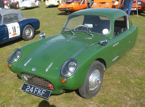 Green three-wheeler with a fixed hardtop on grass, seen from the front left. Opens a larger view