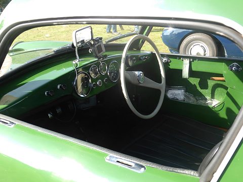 Row of round chrome dials and a white steering wheel in a green dashboard. Opens a larger view