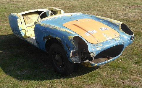 Weathered blue and orange glass-fibre body shell with no wheels or engine, on grass. Opens a larger view