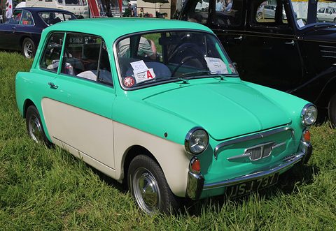 Mint-green small saloon with cream lower panels and a show card in its windscreen, parked on long grass. Opens a larger view