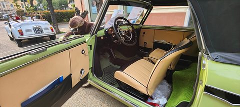 Open door of a lime-green small car showing tan seats, a thin black steering wheel and green floor mats. Opens a larger view