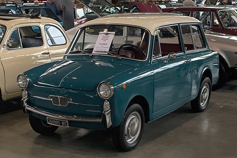 Teal small estate car with a cream roof and a sale card in the windscreen, in a hall of classic cars. Opens a larger view