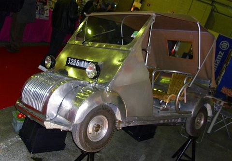 Bare aluminium small open car with a ribbed nose and canvas top on a raised stand. Opens a larger view