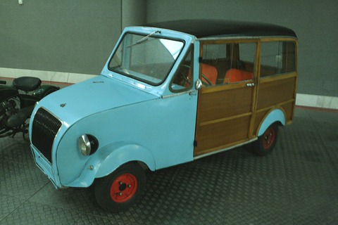 Pale blue small estate car with wooden side panels and doors, black roof, red wheels and a dark vertical-bar grille. Opens a larger view