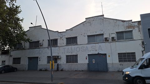 Long whitewashed industrial building with a stepped gable, barred windows and blue doors, a white van parked at the right. Opens a larger view