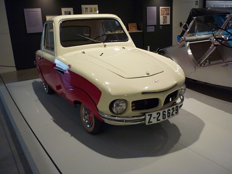 Cream and red two-tone coupé with a hardtop, twin grille openings and round headlamps, on a white museum floor.