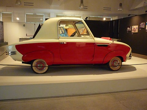 Side view of a small two-tone coupé, red lower body and cream roof and nose, whitewall tyres with red wheels. Opens a larger view
