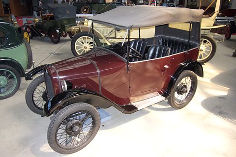A maroon open tourer with a beige hood, black wings and wire wheels among other veteran cars. Opens a larger view
