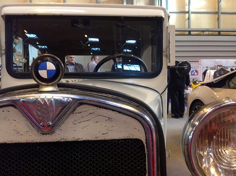 Close view of a BMW roundel on a stalk above a chrome radiator shell with a triangular emblem. Opens a larger view
