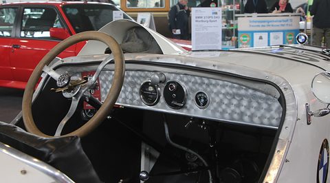 A thin wooden steering wheel before an engine-turned aluminium panel with three round gauges. Opens a larger view