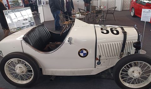 Side view of a white sports two-seater with a strapped bonnet, BMW roundel and white wire wheels. Opens a larger view
