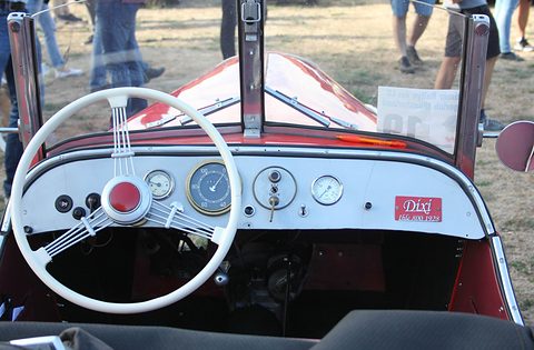 A white four-spoke steering wheel before a cream dashboard with round gauges and a Dixi plaque. Opens a larger view