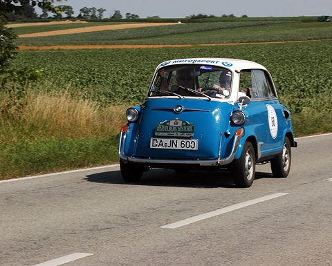 Blue and white bubble car with rally plate number 68 driving towards the camera on a country road between fields. Opens a larger view
