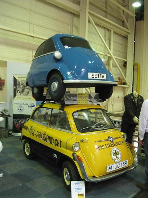 Yellow and black small car with ADAC lettering and eagle badge, a blue bubble car mounted on its roof rack. Opens a larger view