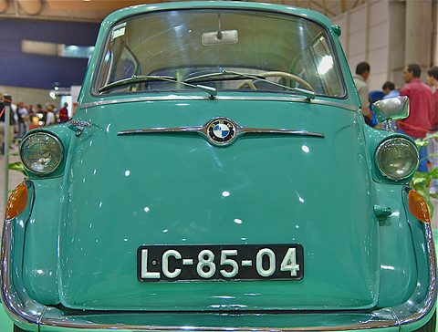 Front of a sea-green bubble car with two round headlamps, amber indicators and a black and white plate. Opens a larger view