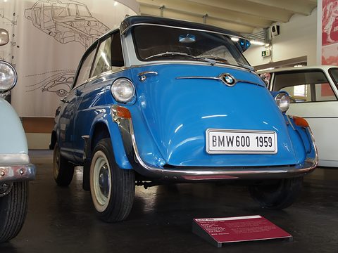 Low front view of a blue bubble car with white roof, chrome bumper, whitewall tyres and a museum sign on the floor. Opens a larger view