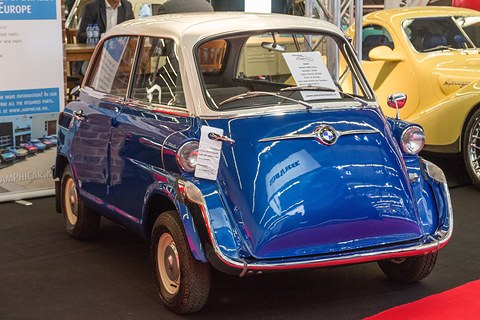 Glossy blue bubble car with white roof on a red carpet, sale cards in the windscreen, a yellow car behind. Opens a larger view