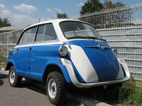 Blue and white bubble car beside a white mesh fence, round headlamps, chrome strip and roundel, knobbly tyres. Opens a larger view