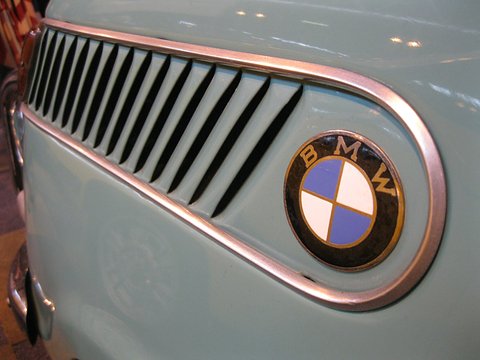Close view of a chrome-edged slotted air intake and a blue and white enamel roundel on pale blue paint. Opens a larger view