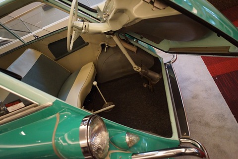 Pale green steering column hinged to the door with a jointed rod down to the floor, grey bench, gear lever, dark carpet. Opens a larger view