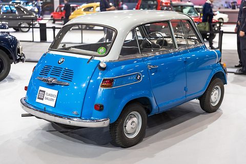 Rear three-quarter of a blue car with pale grey roof on a white floor, louvred engine lid and a show sign. Opens a larger view