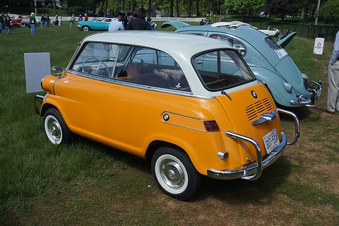 Yellow car with white roof parked on grass, seen from behind and the left, chrome bumper bars and a Minnesota plate. Opens a larger view