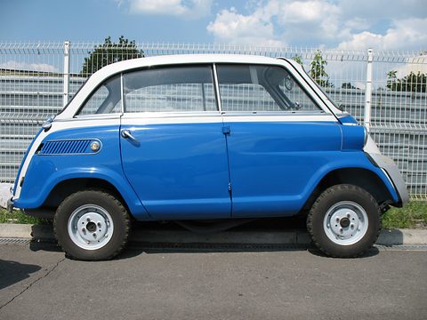 Blue car with white roof and nose parked beside a white mesh fence under a cloudy blue sky. Opens a larger view