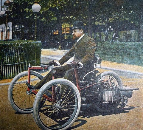 A colour print of a bearded man in a bowler hat on a small red-framed three-wheeled racing car in a park. Opens a larger view
