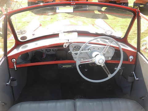 Looking forward over a grey bench seat to a white steering wheel and red-trimmed dashboard. Opens a larger view