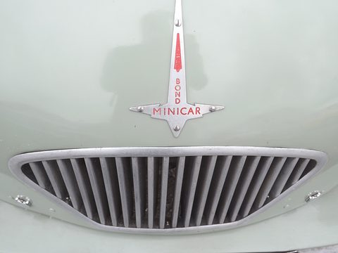 Chrome arrow-shaped badge reading Bond Minicar above a slatted oval grille in pale green paint. Opens a larger view