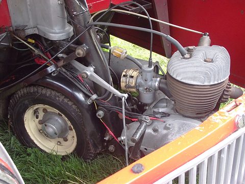 Close view of a finned engine, carburettor and front tyre inside a red body. Opens a larger view