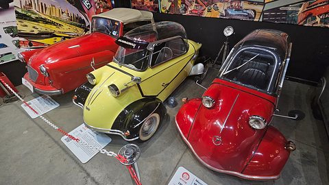 A red three-wheeler, a yellow and black bubble car and a red bubble car in a row behind a chain. Opens a larger view