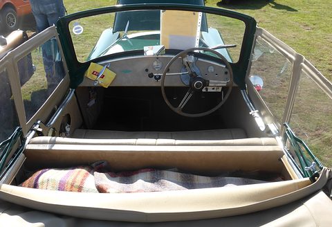 Looking down into an open cockpit with a cream bench seat, rug, steering wheel and painted dash. Opens a larger view