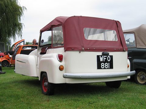 Cream three-wheeler seen from the rear with a maroon hood and rear window, on grass. Opens a larger view