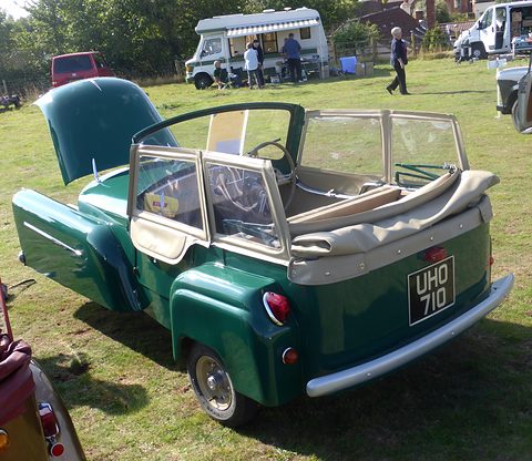 Green open three-wheeler seen from behind with its bonnet up, a camper van beyond. Opens a larger view
