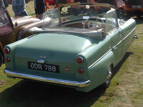Pale green three-wheeler with flared rear wings and tail lamps, seen from behind on grass. Opens a larger view
