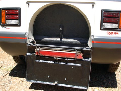 Rear of a white and grey small car with a drop-down flap open on a dark compartment, tail lamps either side. Opens a larger view